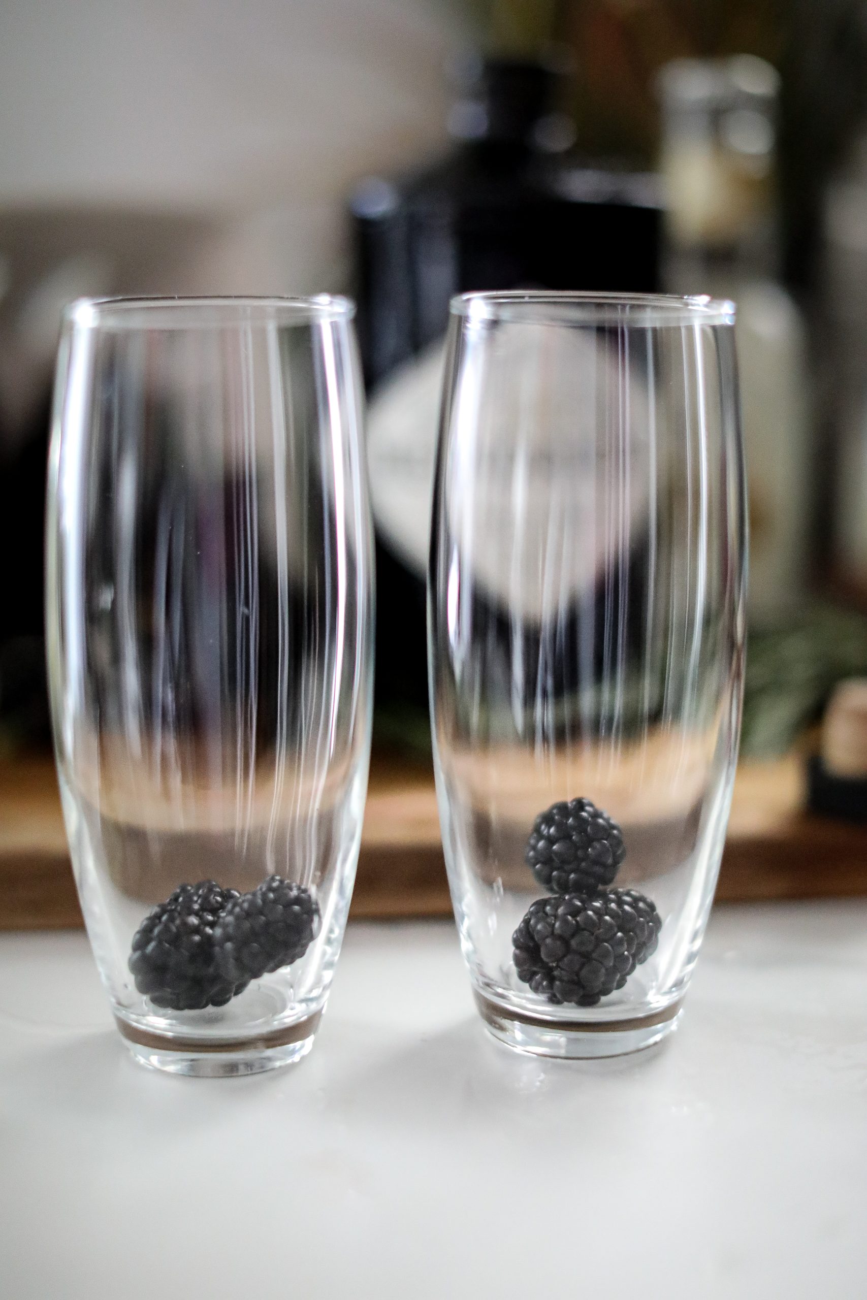 Two tall cocktail glasses with a few blackberries in each glass