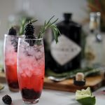 garnished blackberry gin and tonics near a bottle of Hendricks gin