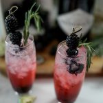 close up of blackberry gin and tonics garnished with fresh berries and rosemary