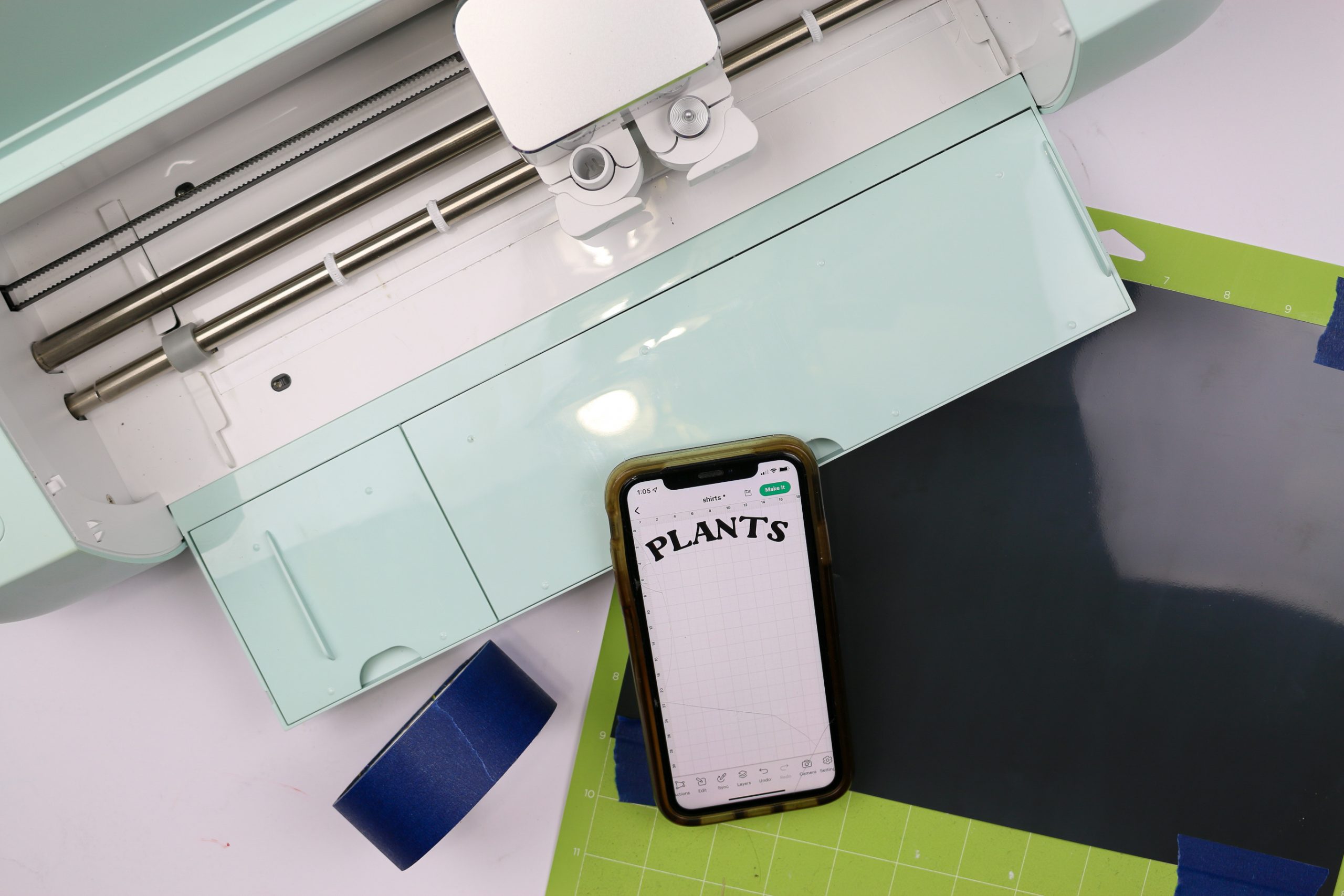 Cricut Explore 3, smartphone, and vinyl on a cutting mat