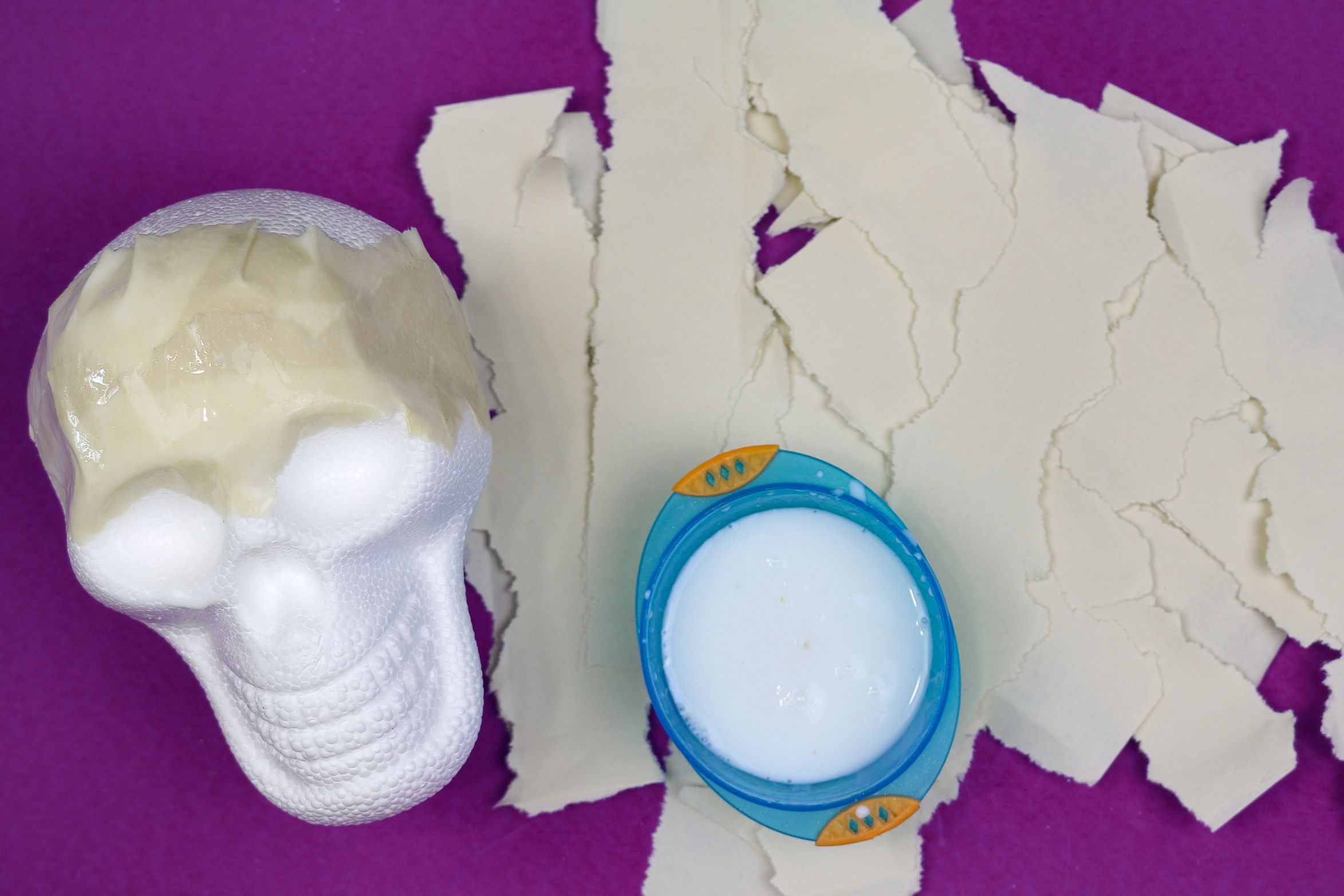 foam skull partially covered with paper mache, ripped construction paper, and white glue on a purple background