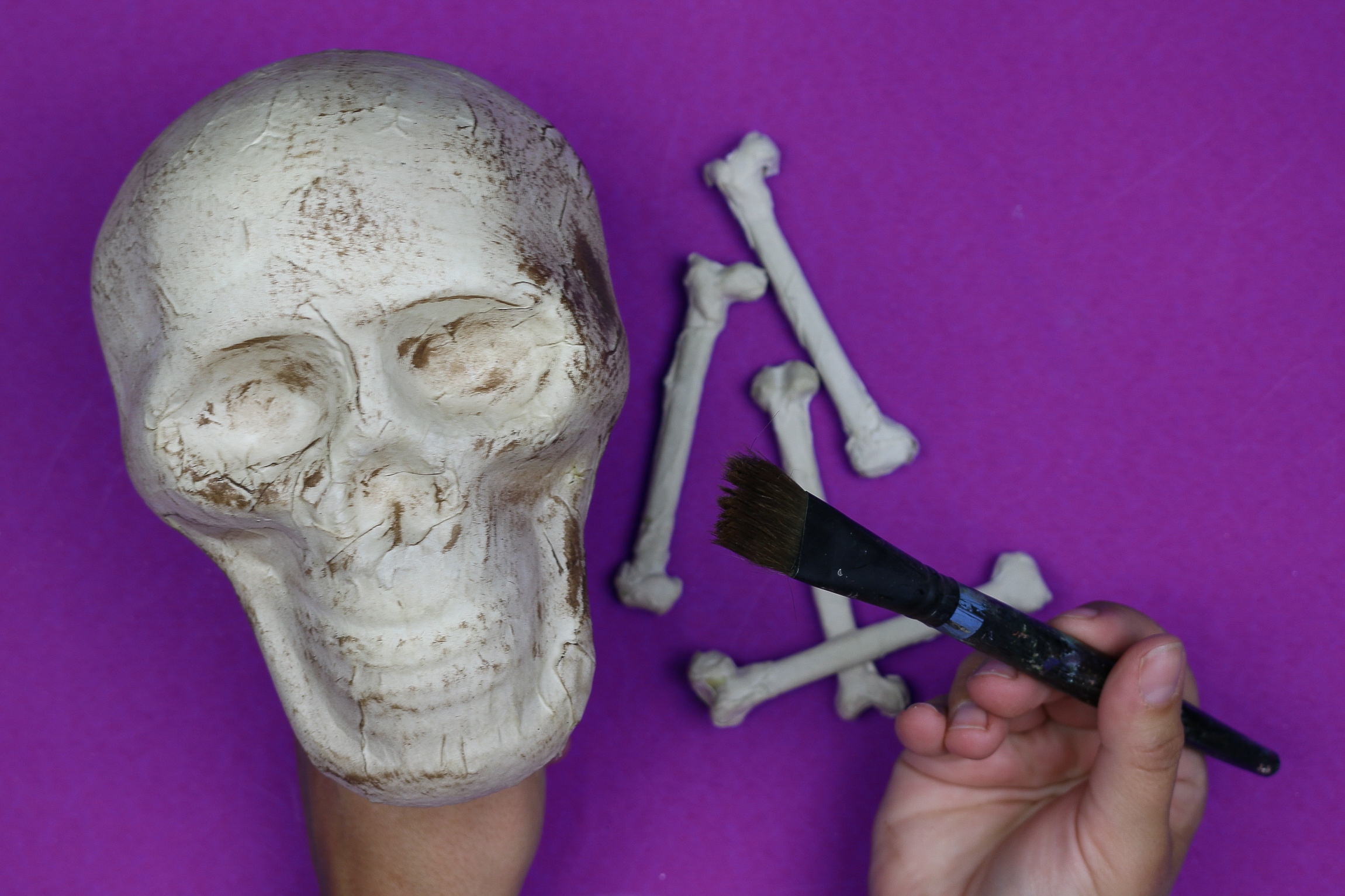 woman's hand applying craft paint to a paper mache skull with a paintbrush
