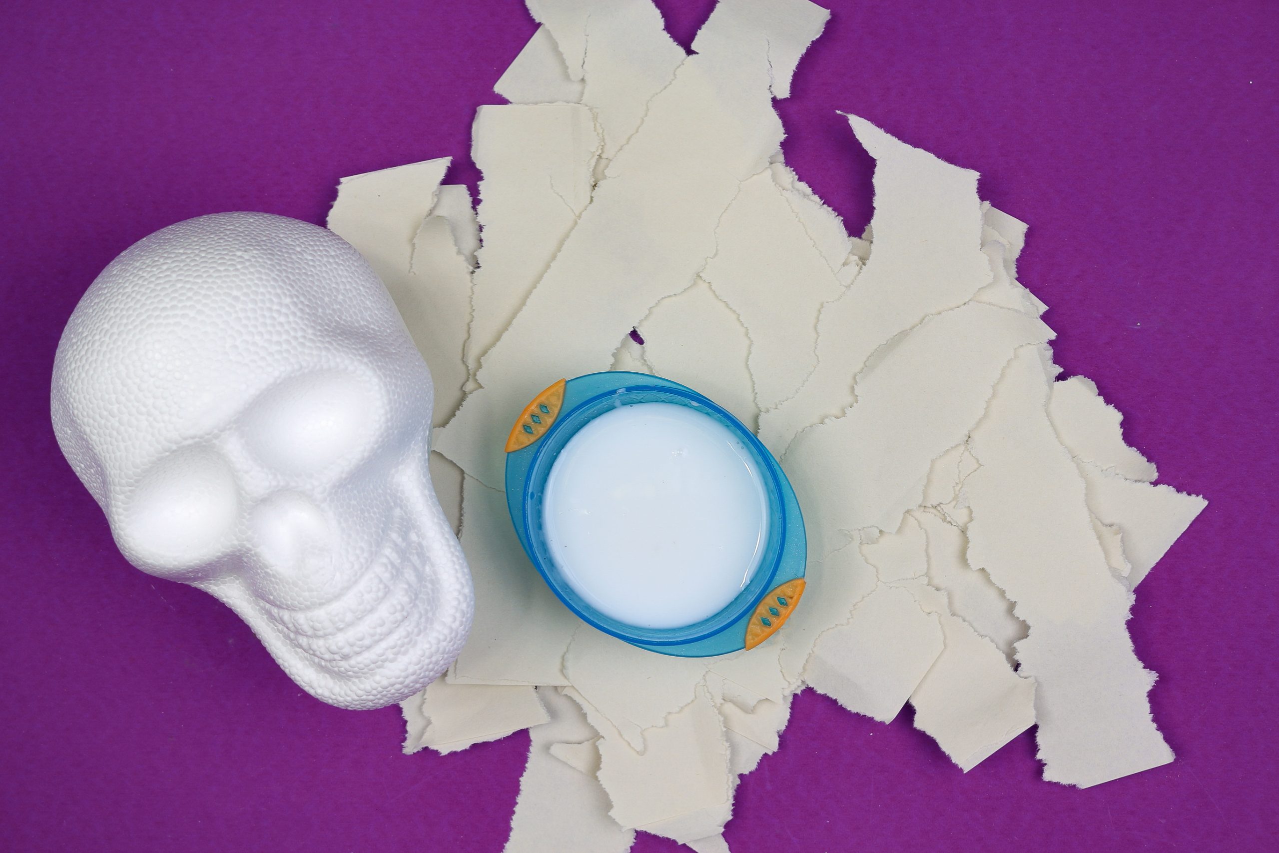 foam skull, ripped construction paper, and diluted white glue on a purple background
