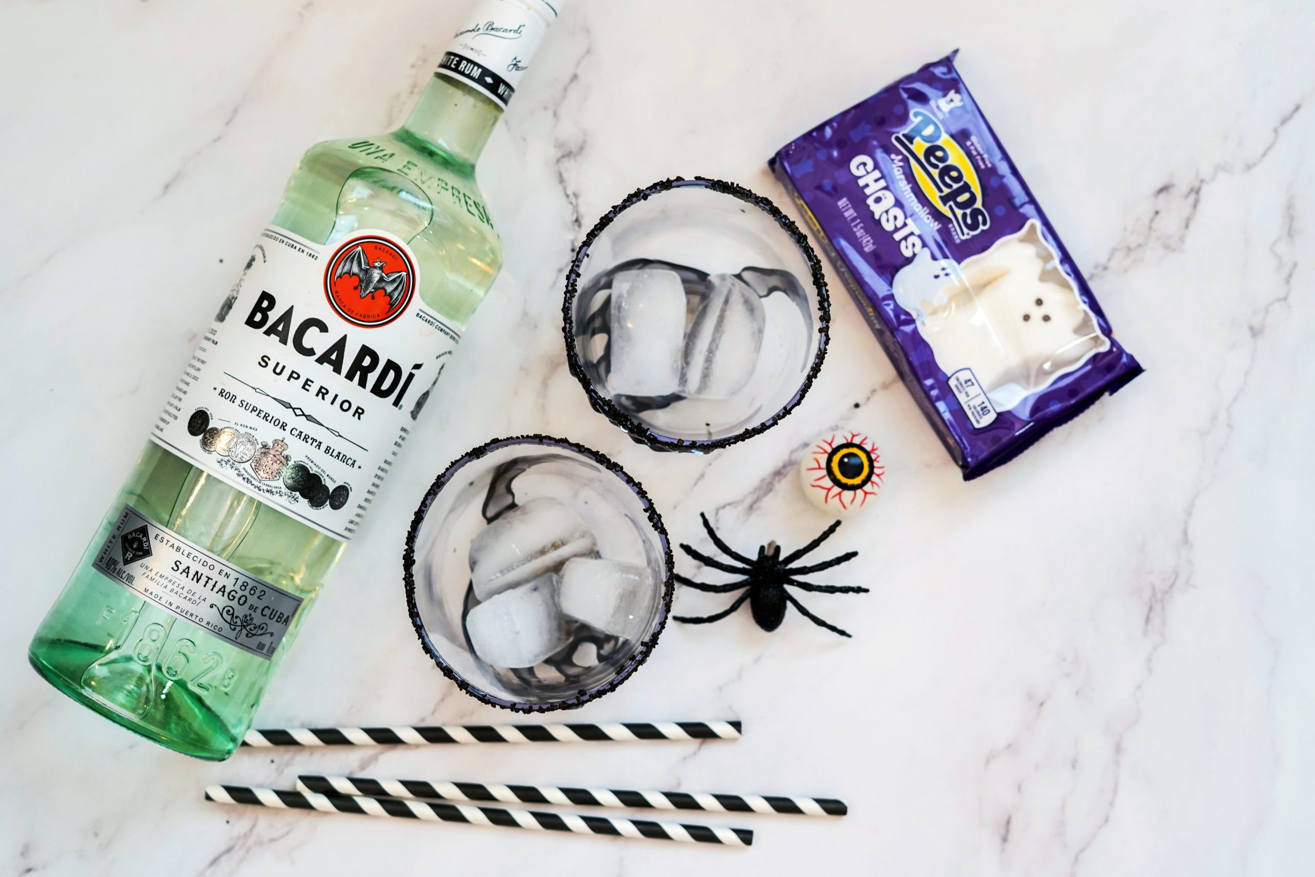 a bottle of run, cocktail glasses, Peeps candy ghosts, and black and white paper straws