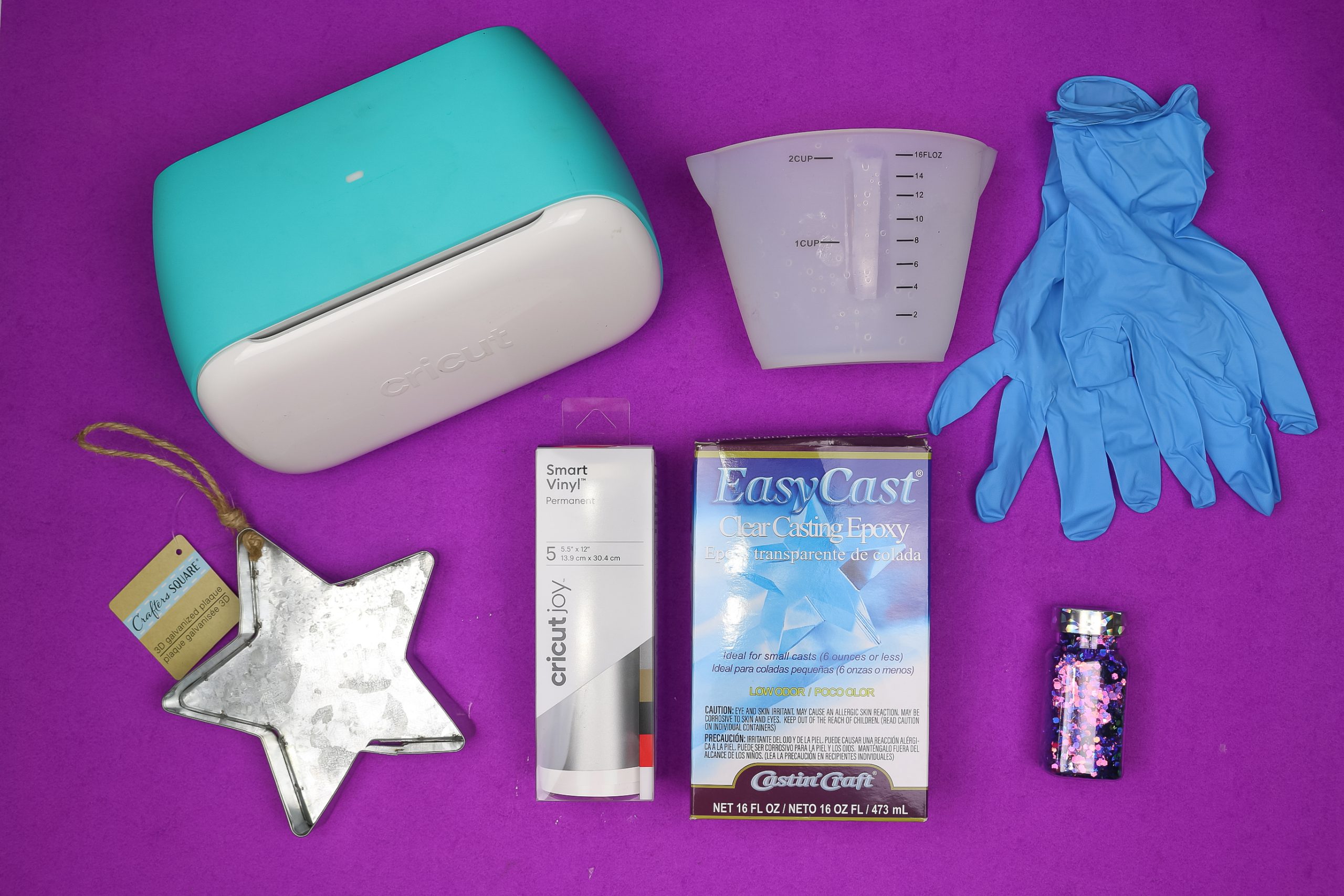 flat lay of the following: Cricut Joy, resin mixing cup, gloves, galvanized metal star tray, Smart Vinyl, EasyCast resin, and chunky purple glitter