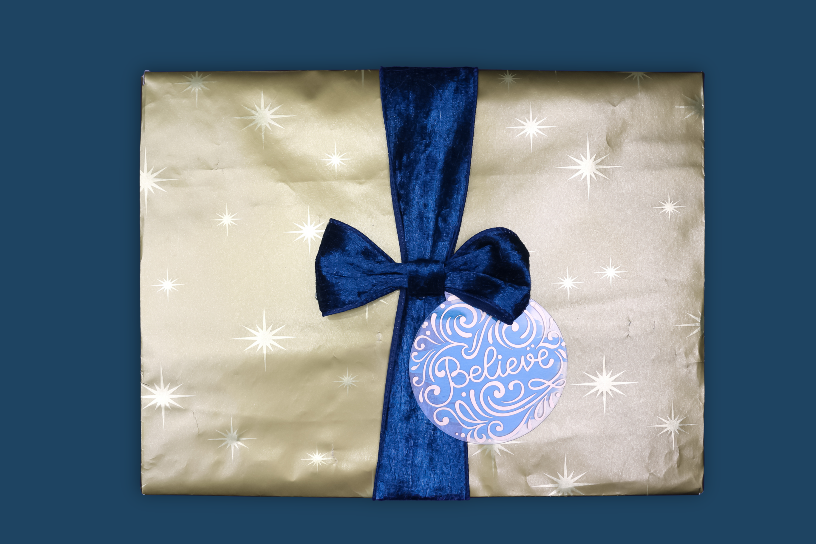 present wrapped with gold paper and a blue ribbon with a blue glitter acrylic gift tag