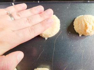 woman's hand pressing sugar cookie dough onto a cookie sheet
