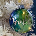 blue and green marbled circle ornament with the word Bright in gold vinyl hanging on a white tree