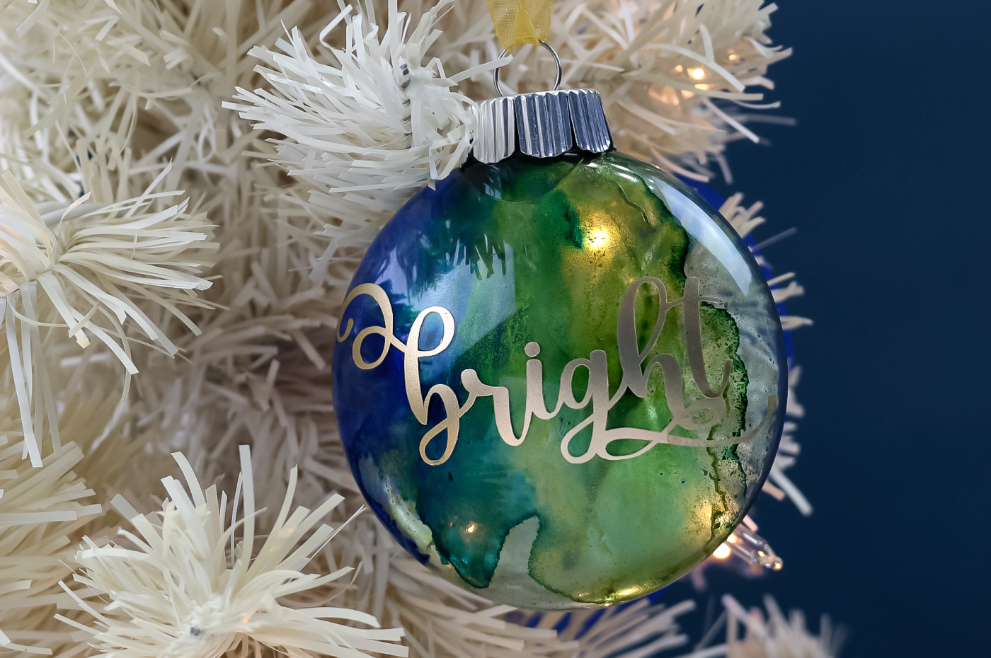 blue and green marbled circle ornament with the word Bright in gold vinyl hanging on a white tree