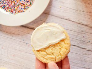 hand holding a sugar cookie half frosted with white frosting