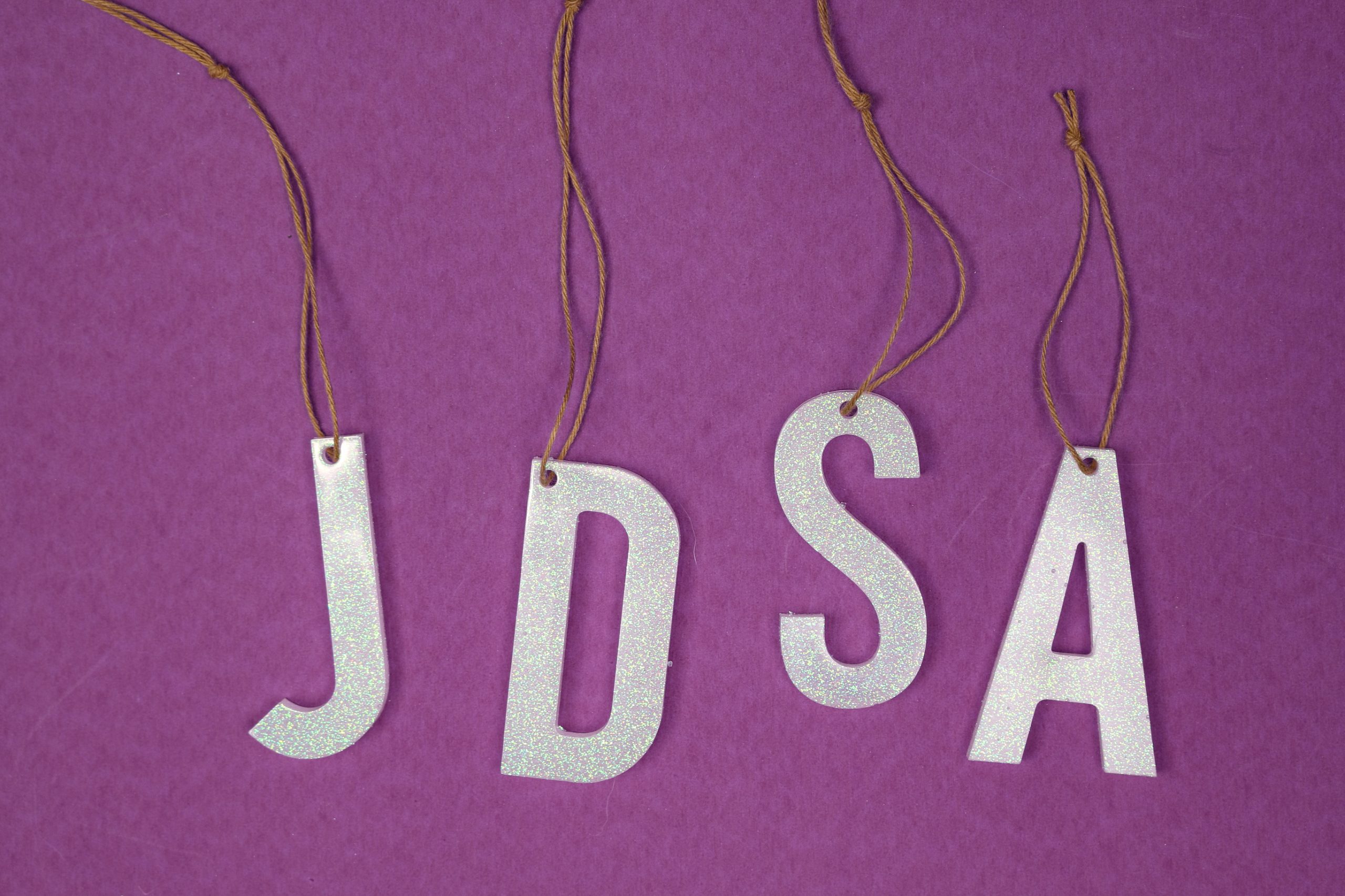 four resin stocking marker letters with twine hangers on a purple backgroun
