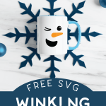 winking snowman mug laying on a blue paper snowflake