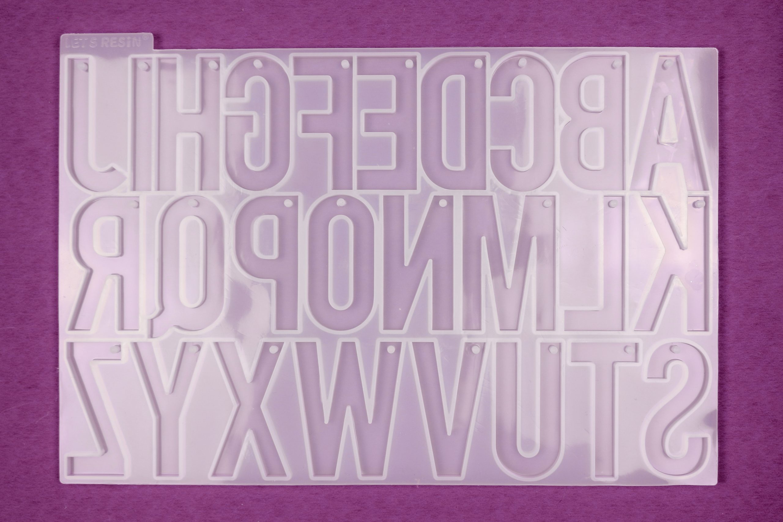 an empty silicone alphabet mold on a purple background