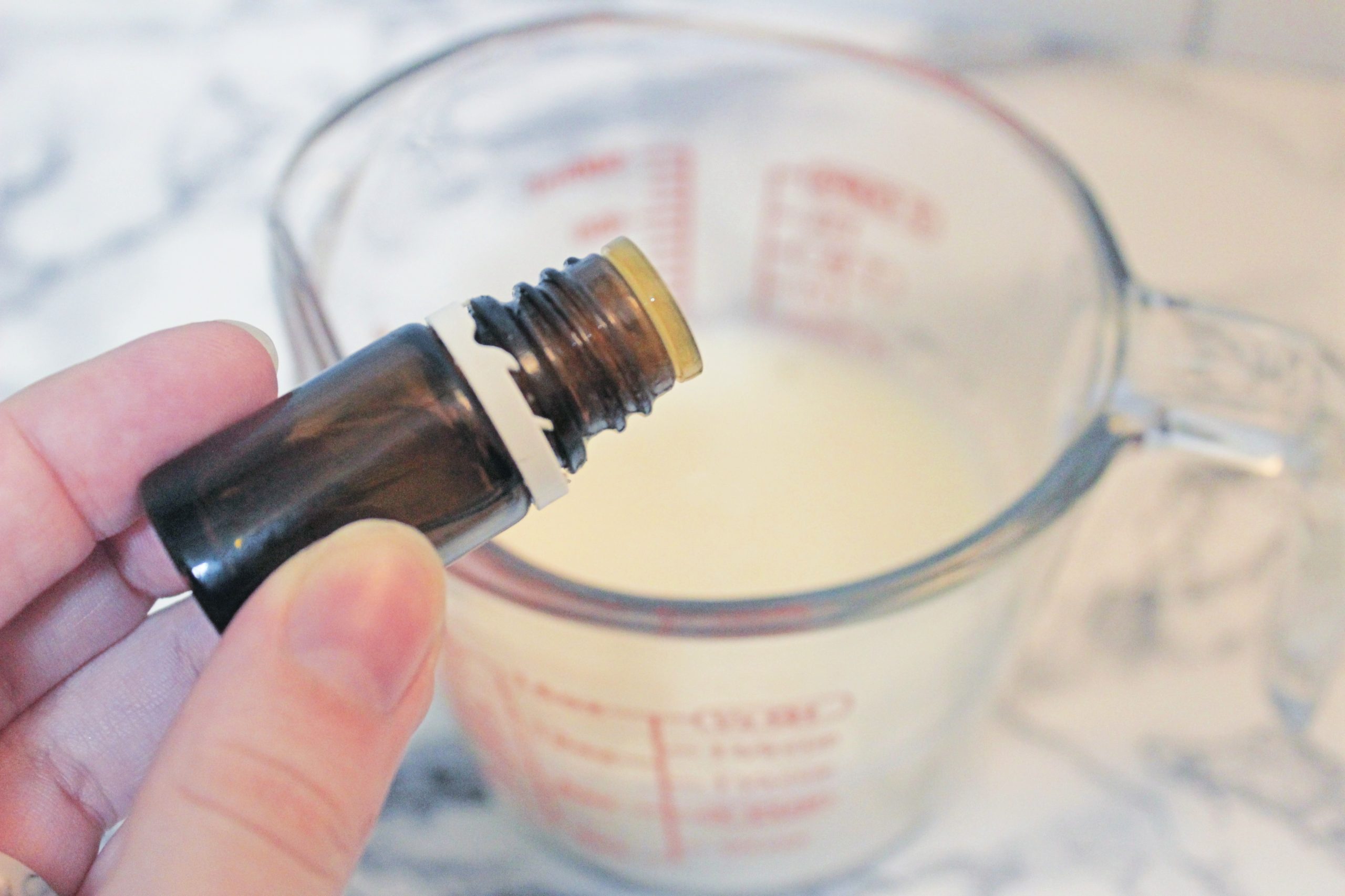 hand putting essential oils into a measuring cup of melted melt and pour soap