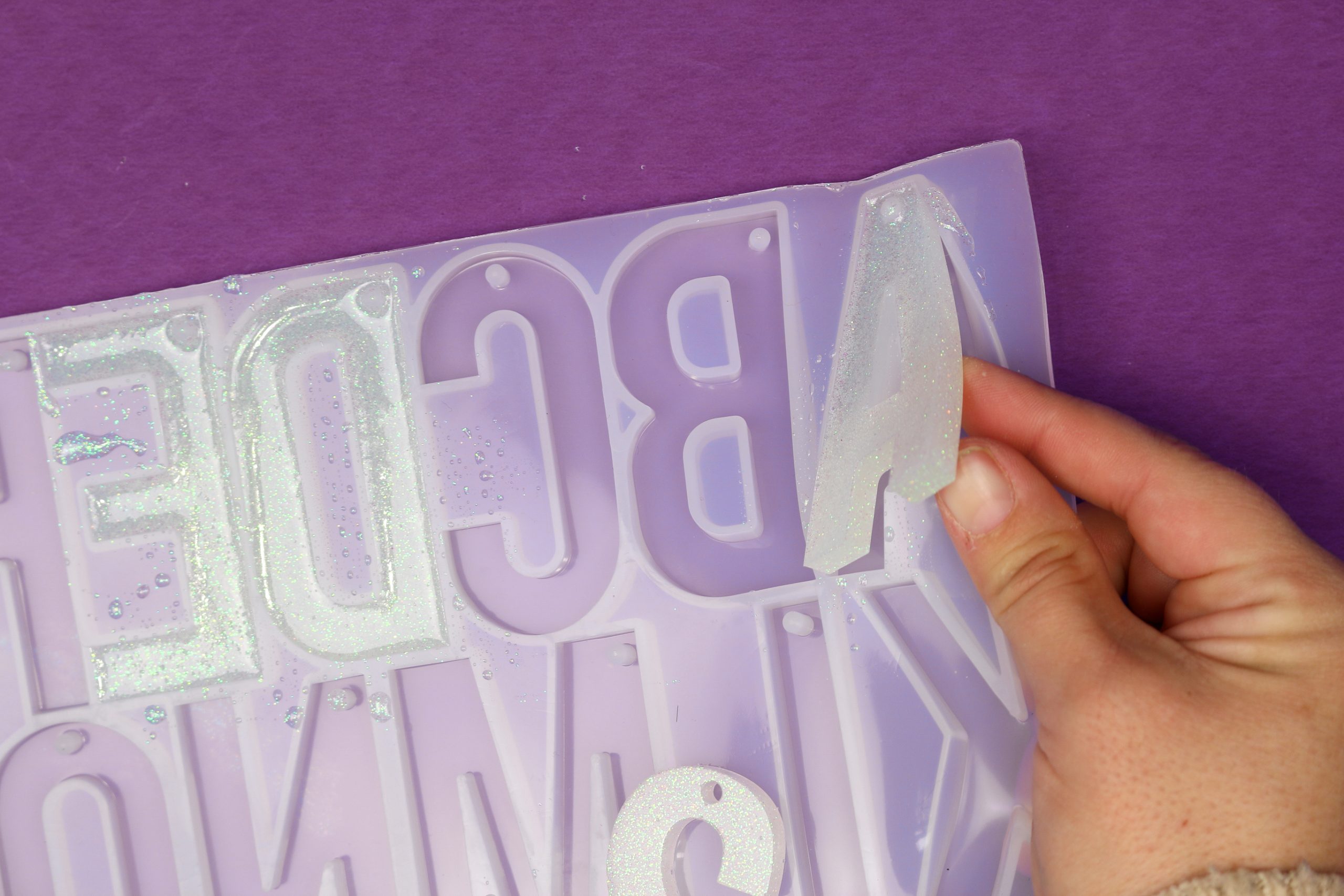 white woman's hand removing a resin letter from a silicone alphabet mold