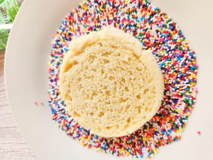 frosted sugar cookie being dunked into sprinkles