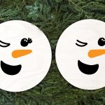 two wooden circle signs with winking snowman faces