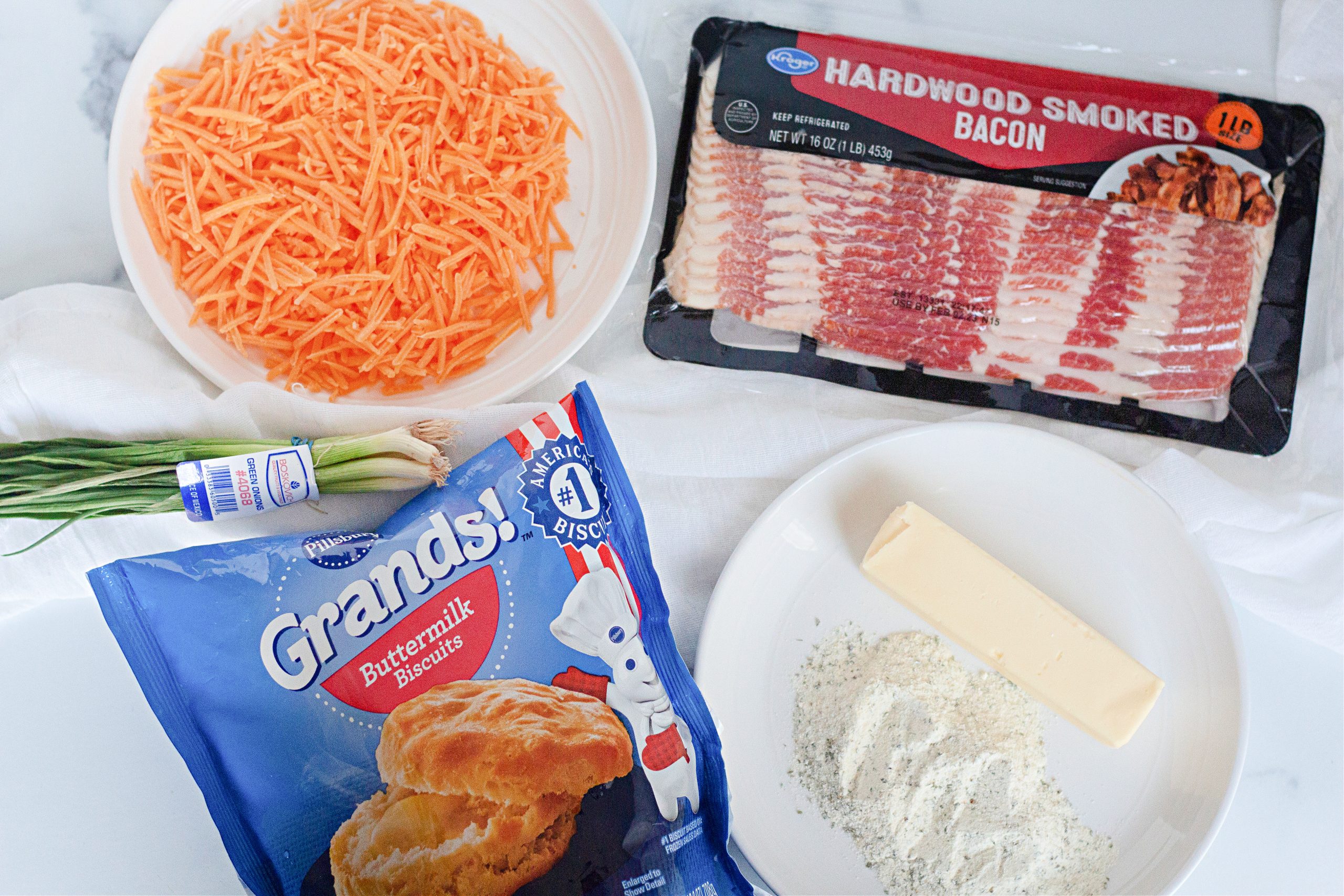 Flay lay photo of shredded cheese, Grands biscuits, butter, and bacon.