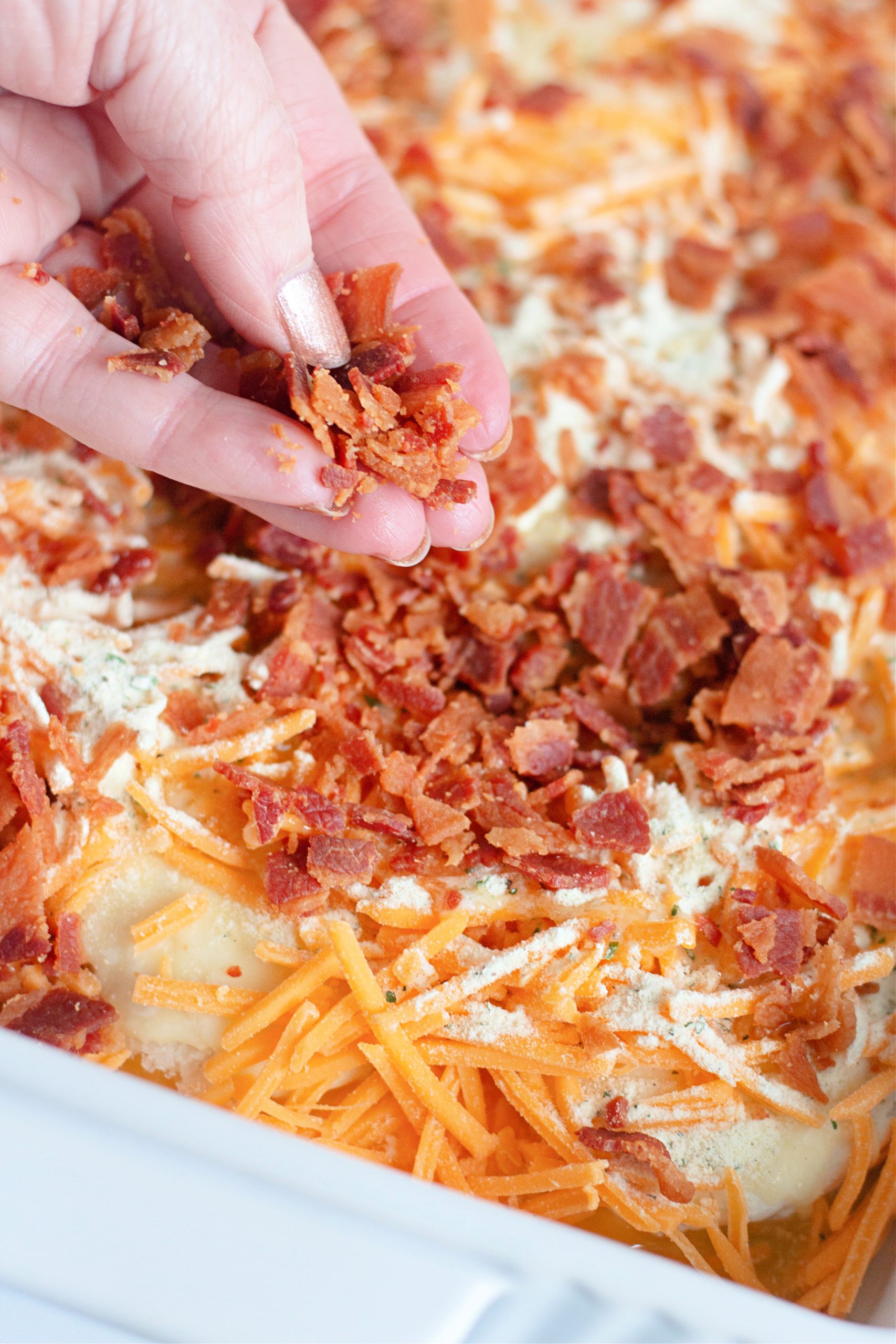 Woman's hand sprinkling crumbled bacon over baked biscuits.