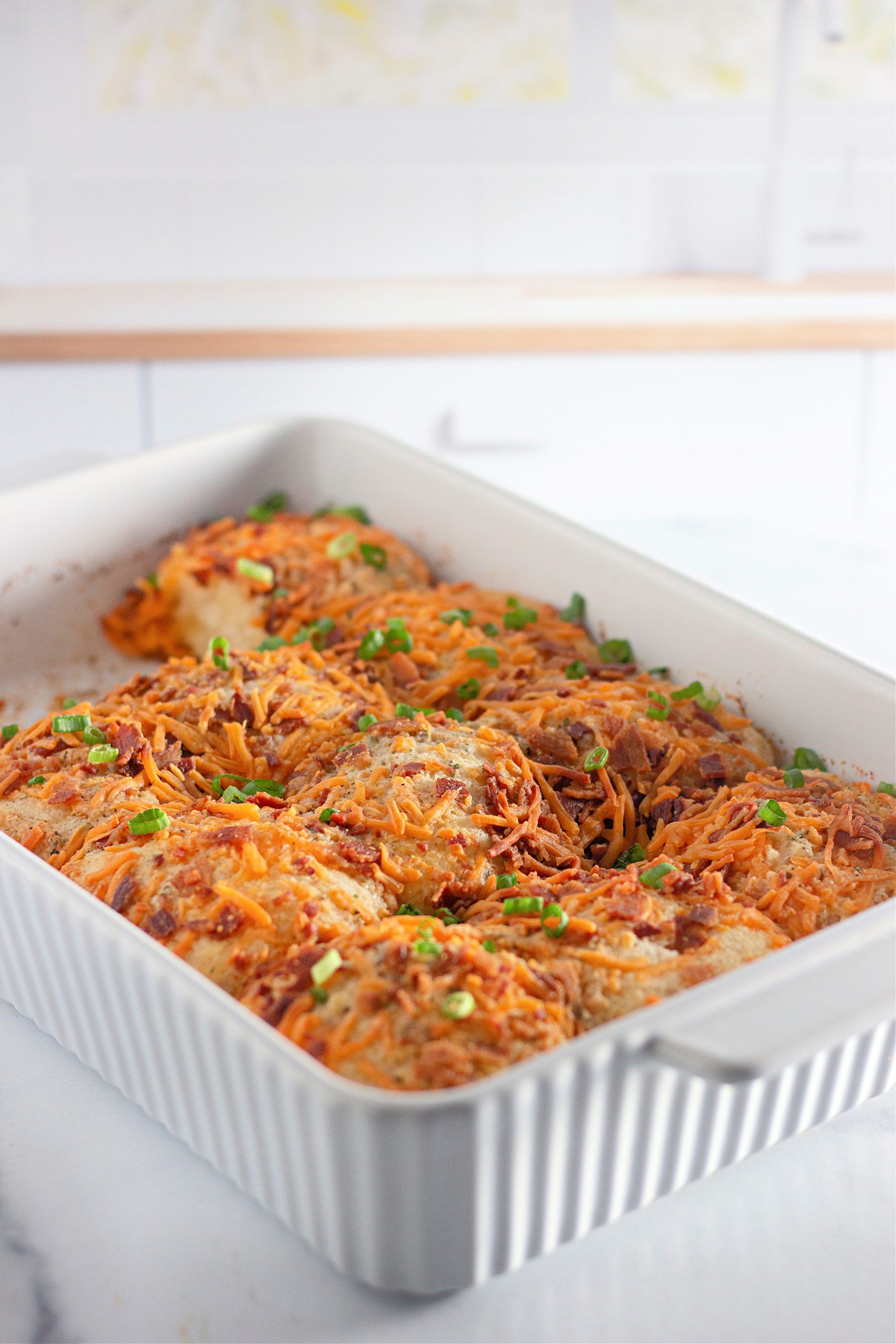 White baking dish filled with Baked biscuits topped with cheese, bacon, and green onions.