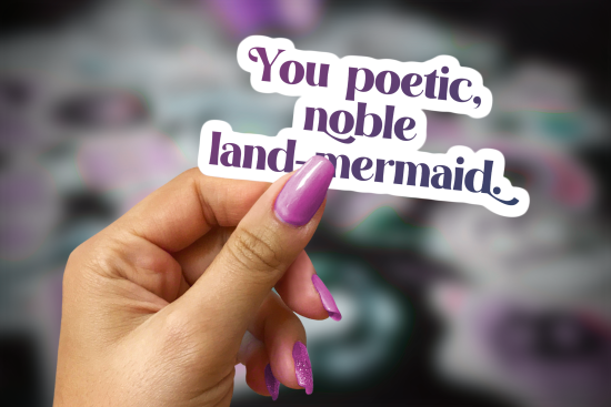woman's hand holding a sticker that reads You poetic, noble land mermaid