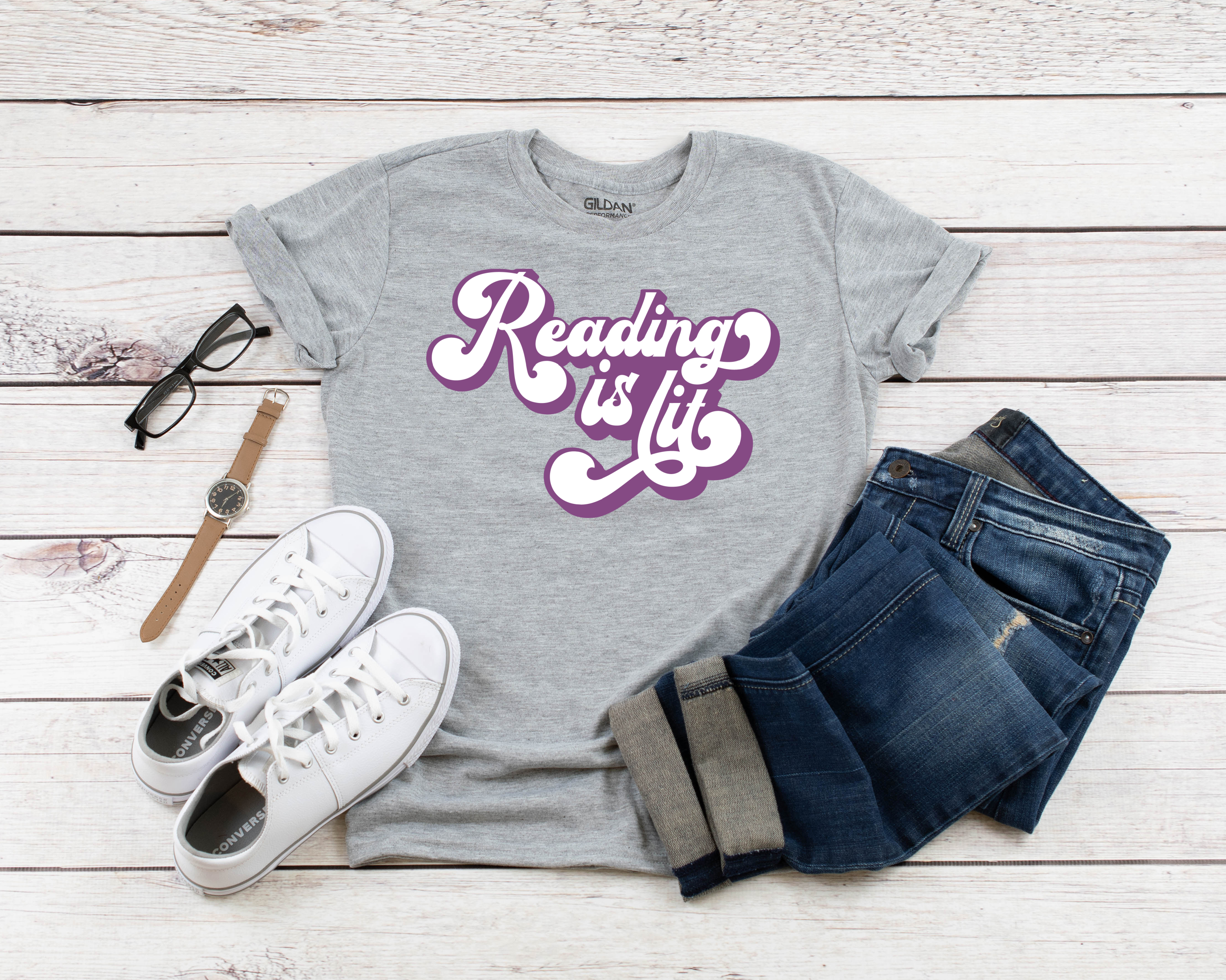 Grey t-shirt with Reading is Lit SVG near jeans, white shoes, glasses and a watch