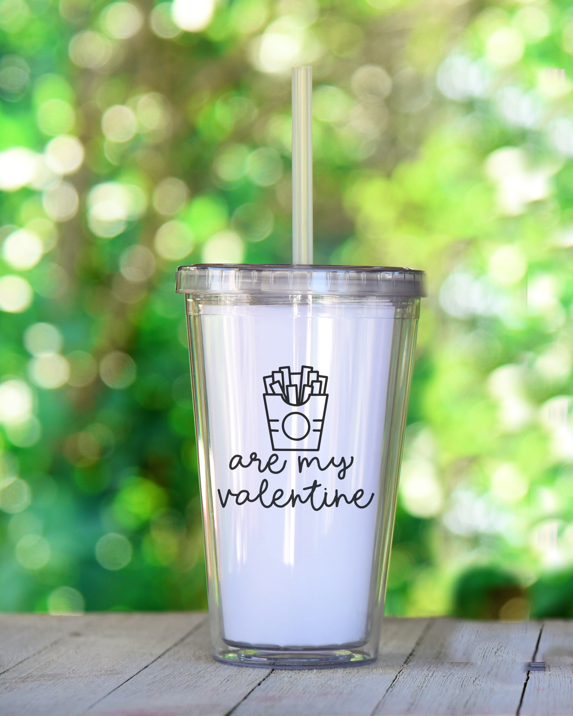 A clear tumbler with Fries Are My Valentine design that is sitting on an outdoor table.