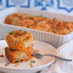 Two baked biscuits topped with cheese, bacon, and green onions on a plate.