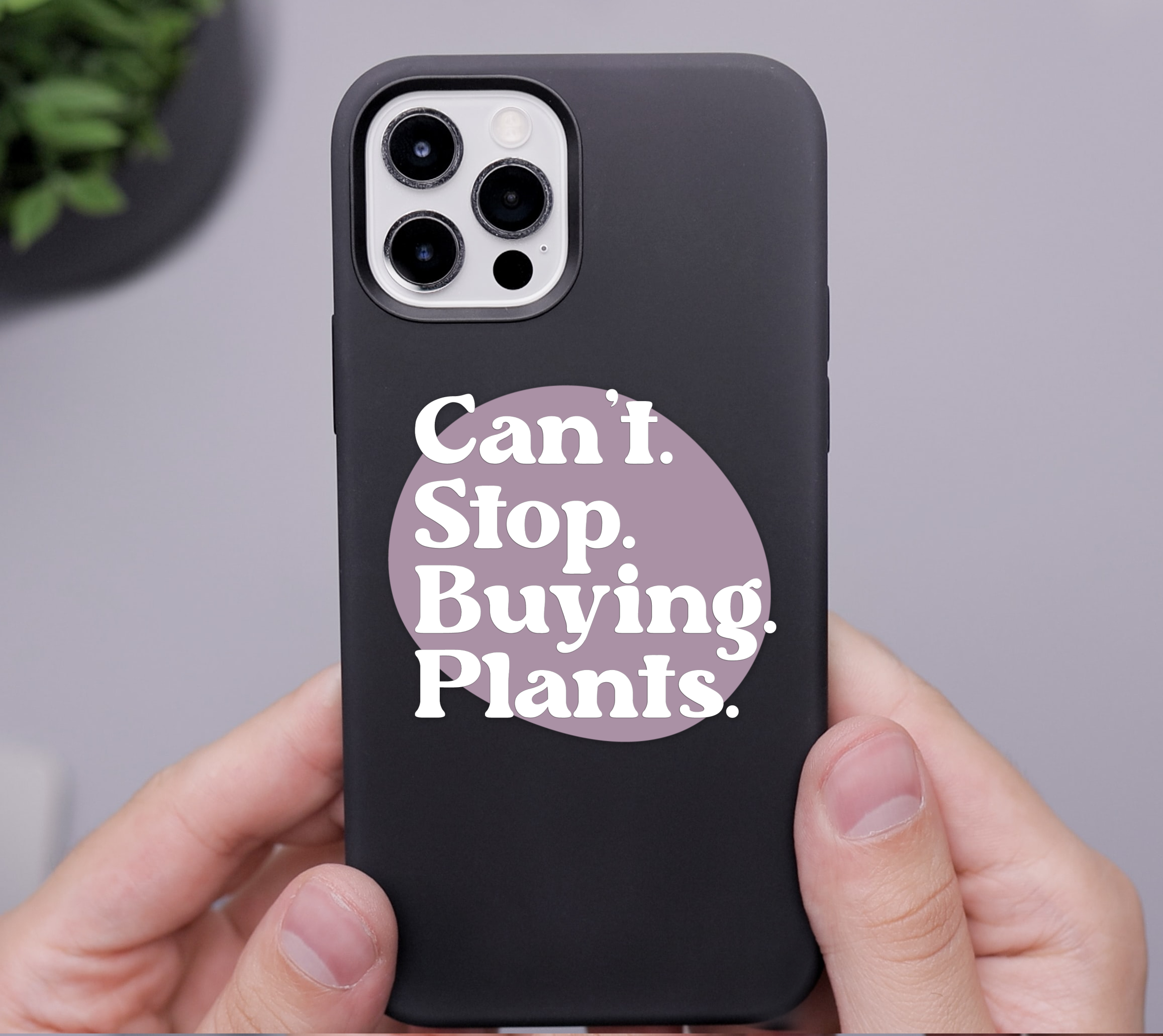 White man's hands holding an iPhone with a Can't Stop Buying Plants sticker on the case.