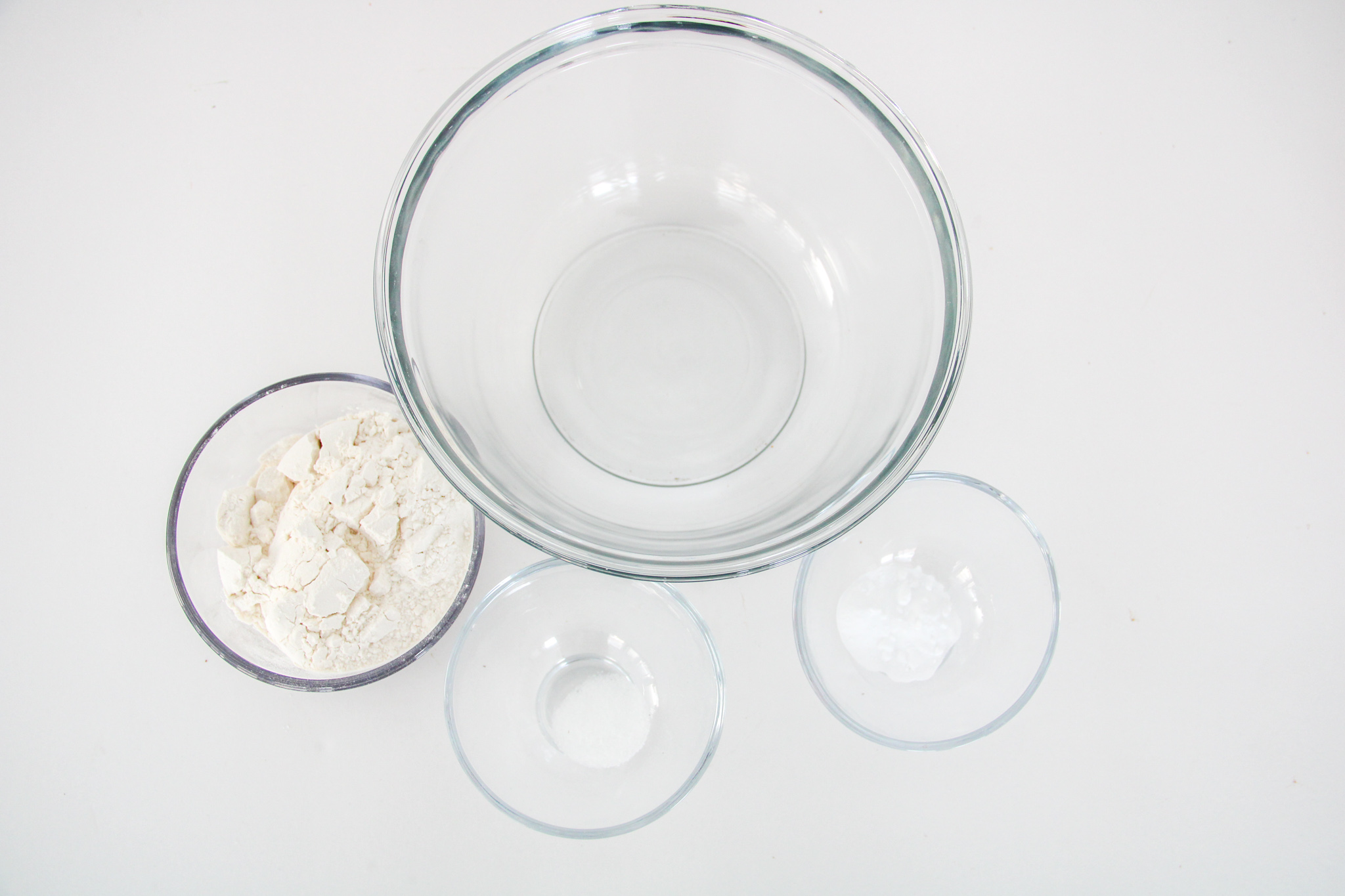 Emptry glass bowl and smaller glass bowls of flour, salt, and baking soda