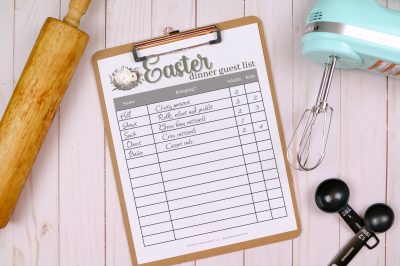A clipboard holding an Easter dinner guest list printable with writing on it. The clipboard is near baking tools