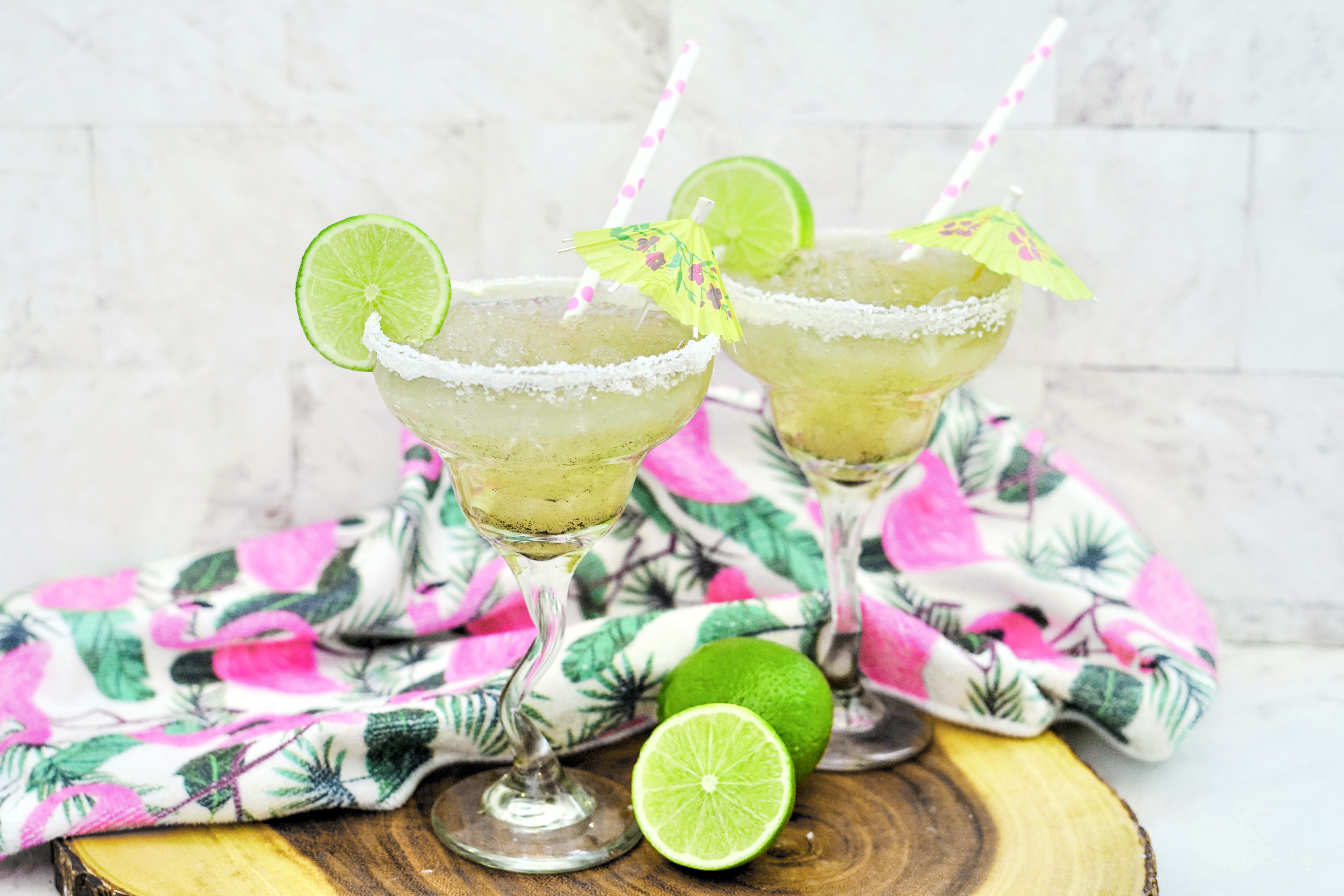 Two frozen lime margaritas with salt rims have been garnished with lime and a small umbrella.
