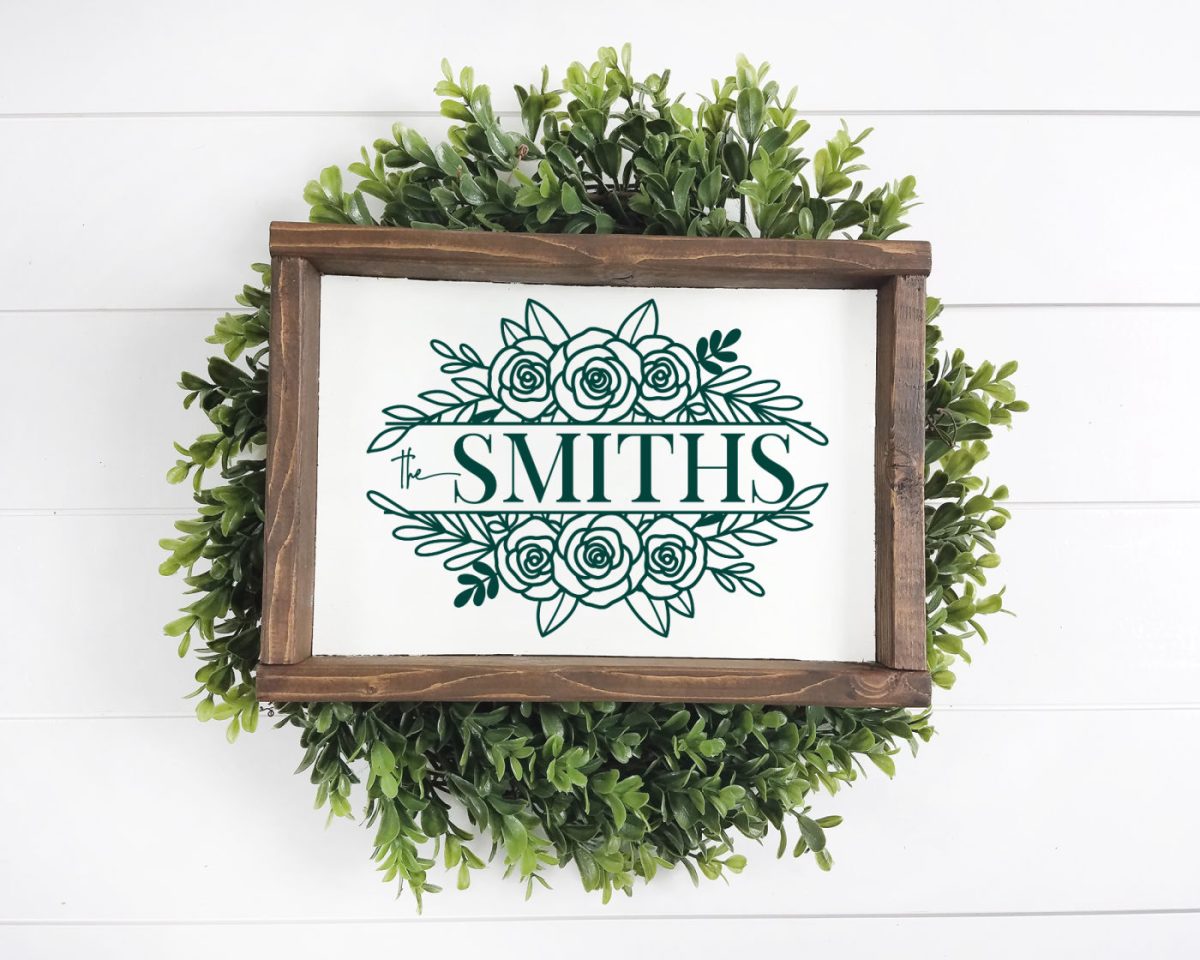 A family name sign in a wooden frame that is resting on a green wreath.