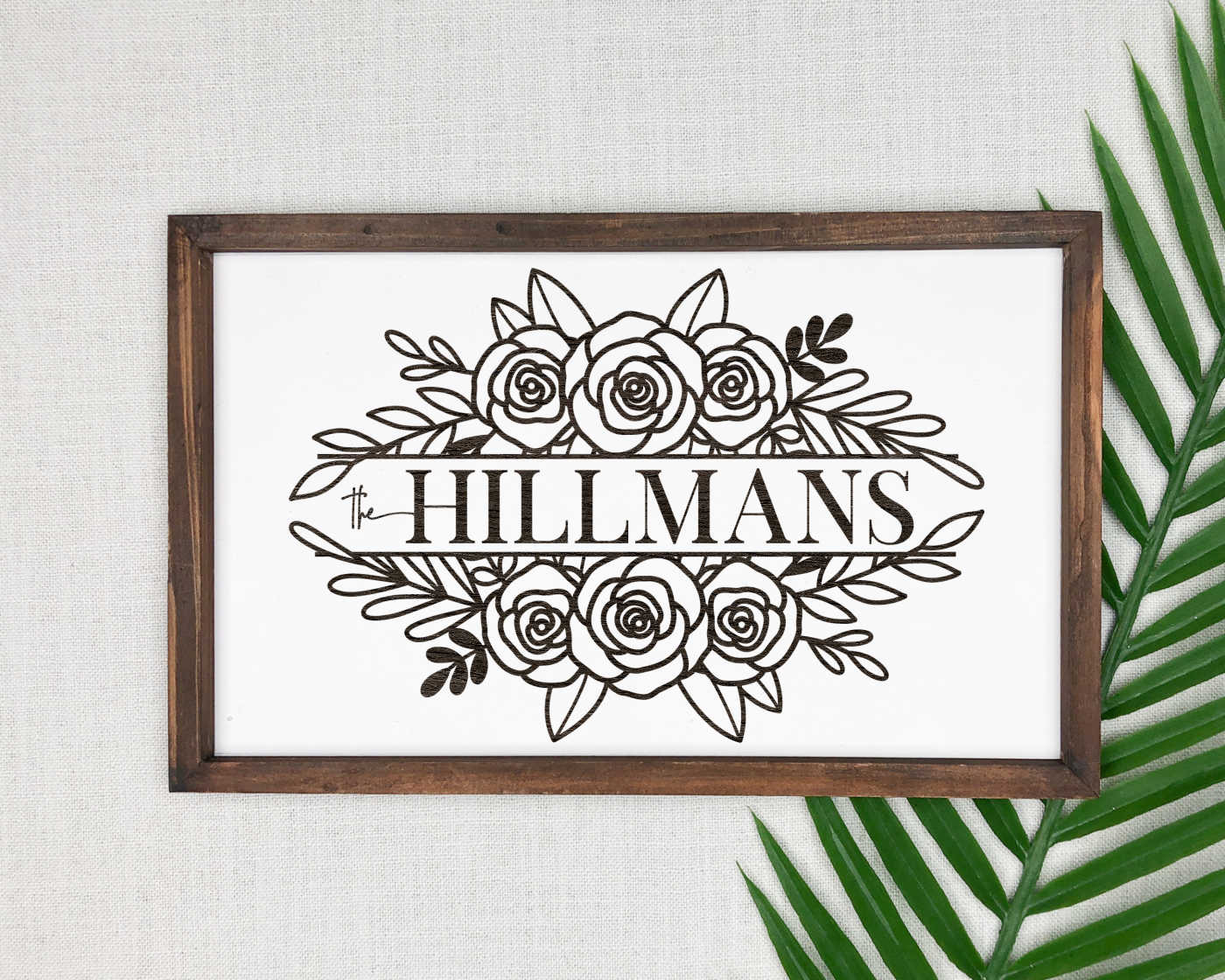 A family name sign in a wooden frame next to a palm branch.