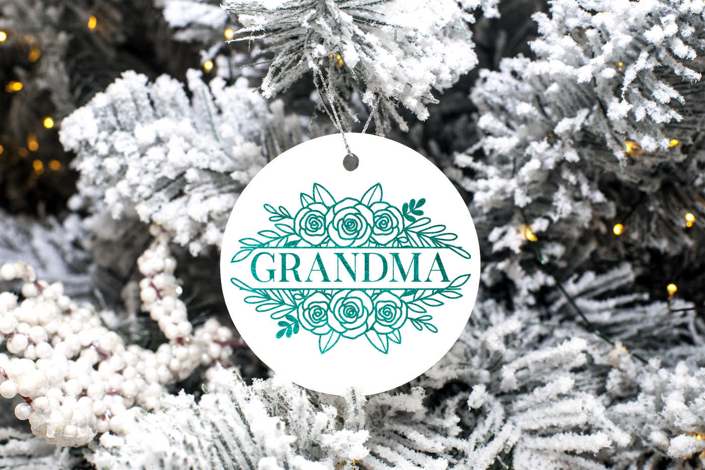 A floral name SVG on a white circle ornament hanging from a flocked tree.