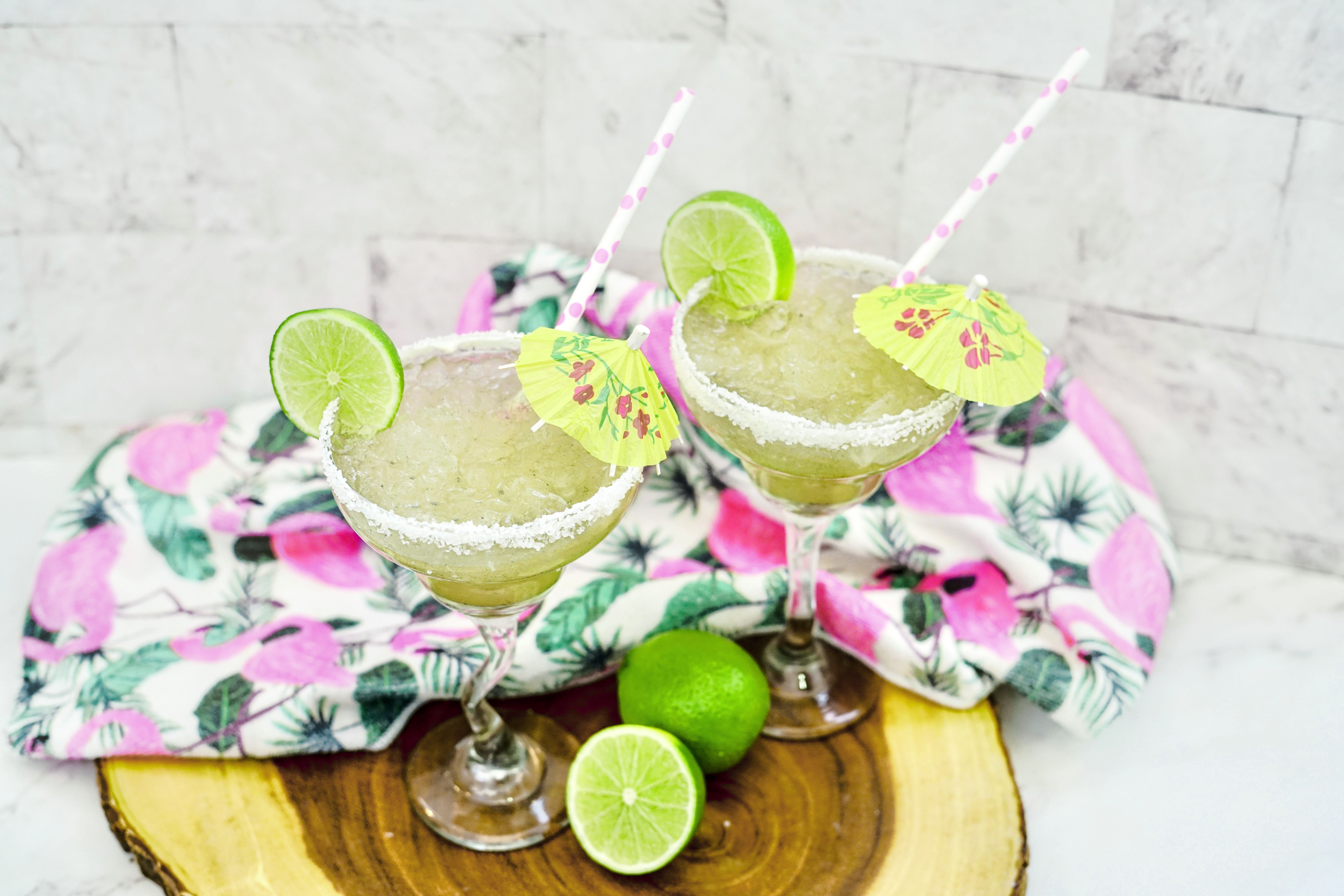 Top down view of frozen lime margaritas with salt rims have been garnished with lime and a small umbrella near limes.