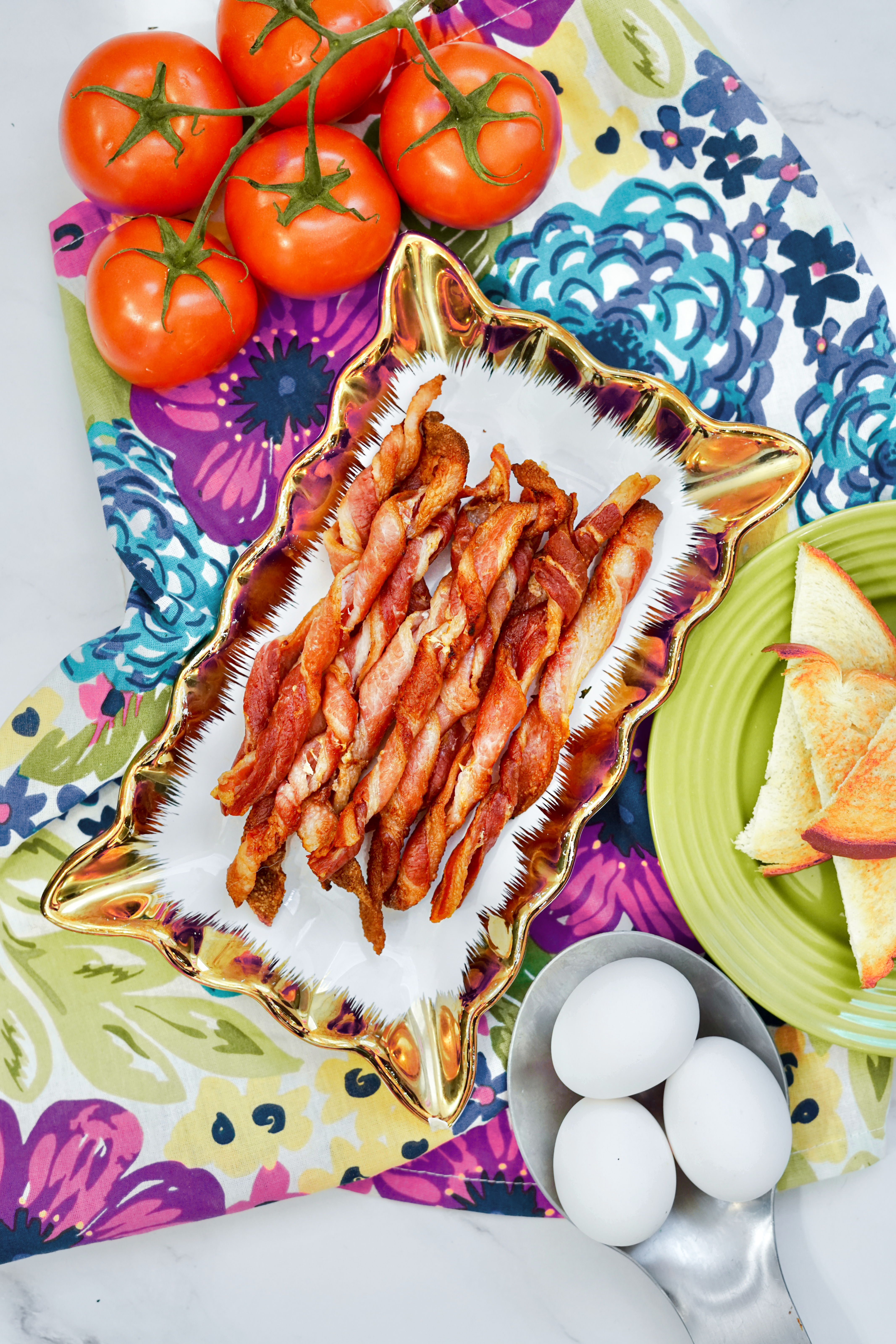 Platter of air fried bacon twists on a colorful tablecloth near tomatoes and eggs.Platter of air fried bacon twists on a colorful tablecloth near tomatoes and eggs.