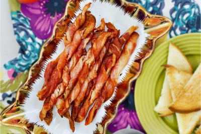 Platter of air fried bacon twists on a colorful tablecloth near tomatoes and eggs.Platter of air fried bacon twists on a colorful tablecloth near tomatoes and eggs.