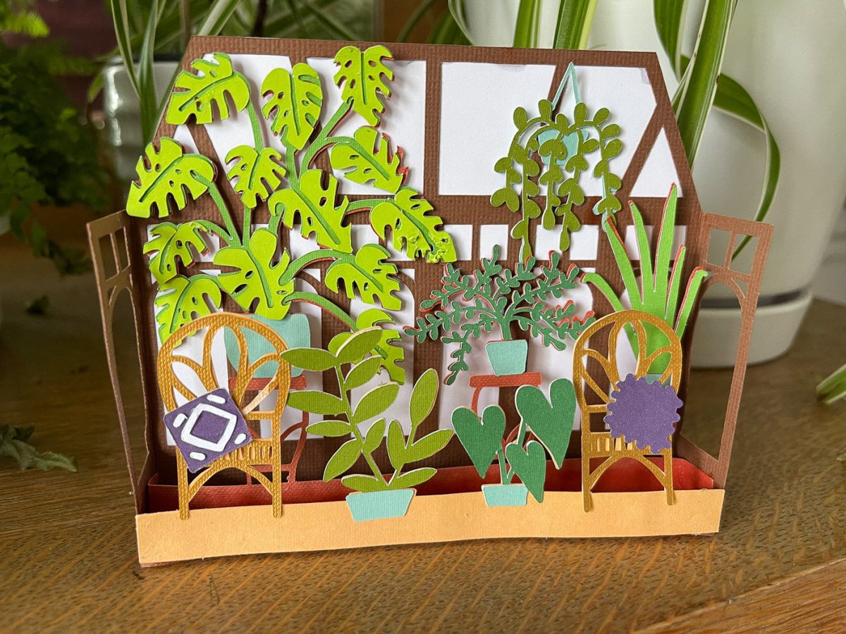 A closeup of 3D Paper Card of houseplants in a sunroom sitting near real plants