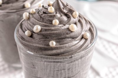 A glass jar is filled with piped and swirled grey stuff dessert topped with white sprinkles