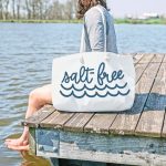 White woman sitting on a lake dock and holding a tote bag that reads Salt-Free