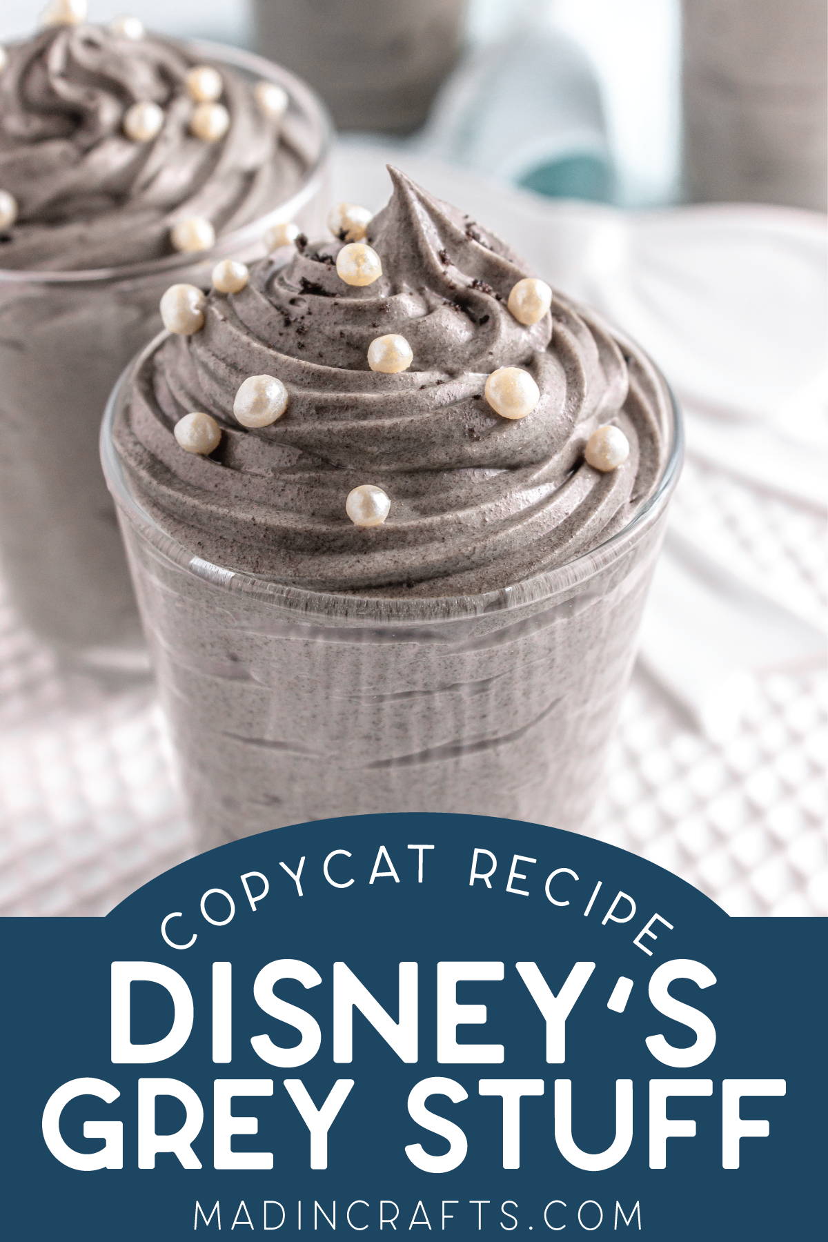 A glass jar is filled with piped and swirled grey stuff dessert topped with white sprinkles