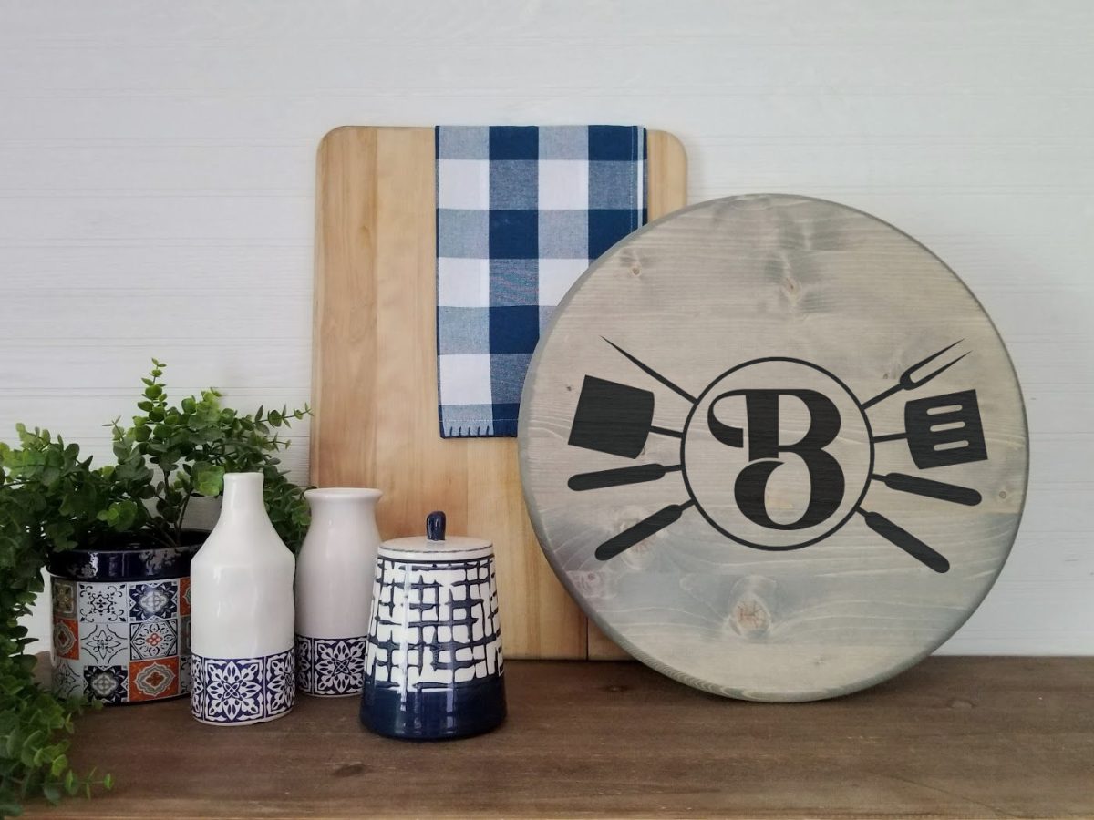 Wooden cutting board with wood burnt grill monogram design near other kitchen decor