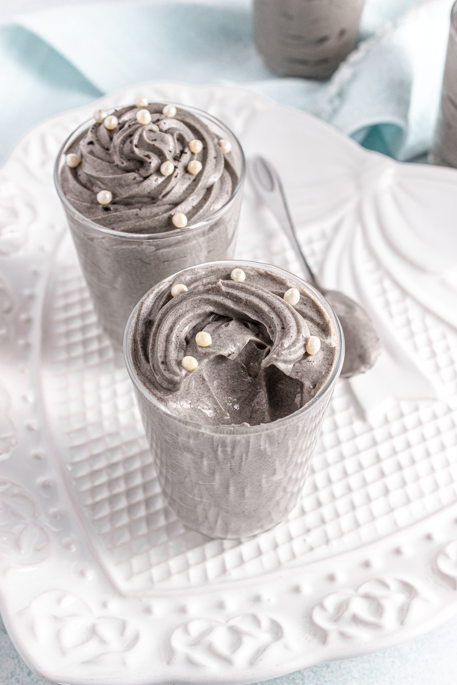 Glass jars are filled with piped and swirled grey stuff dessert topped with white sprinkles. One of the desserts has a spoonful removed from it