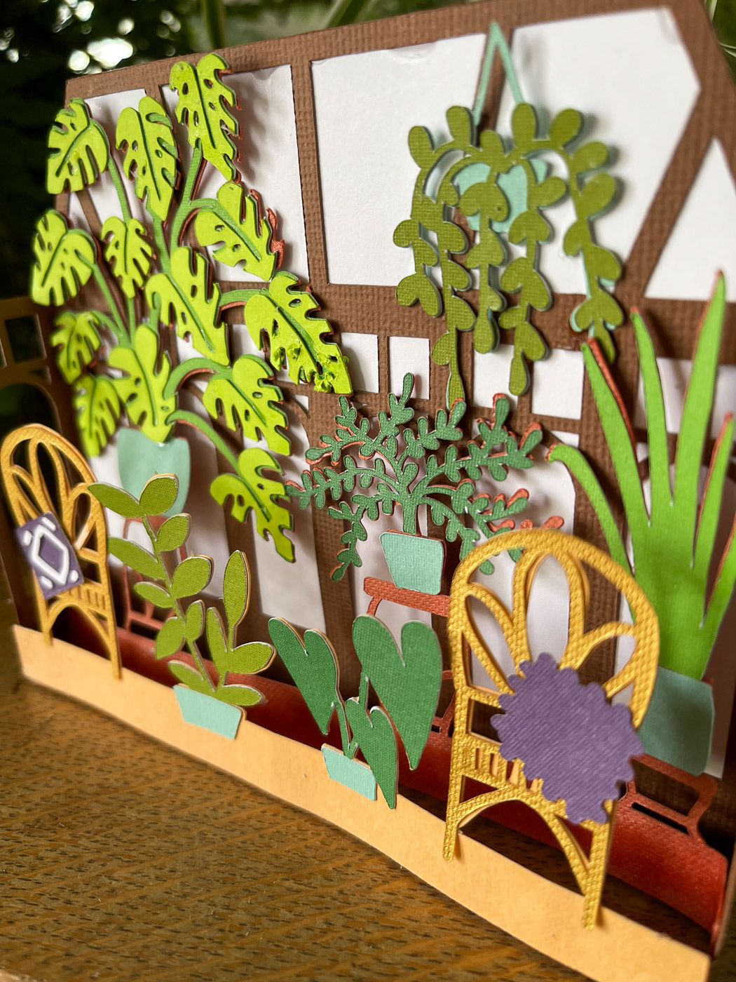 Right side view showing the layers of a 3D Paper Card of houseplants in a sunroom sitting near real plants