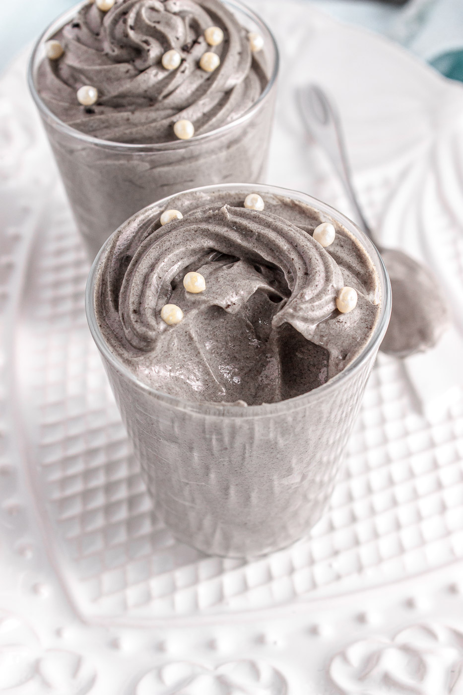 Glass jars are filled with piped and swirled grey stuff dessert topped with white sprinkles. One of the desserts has a spoonful removed from it