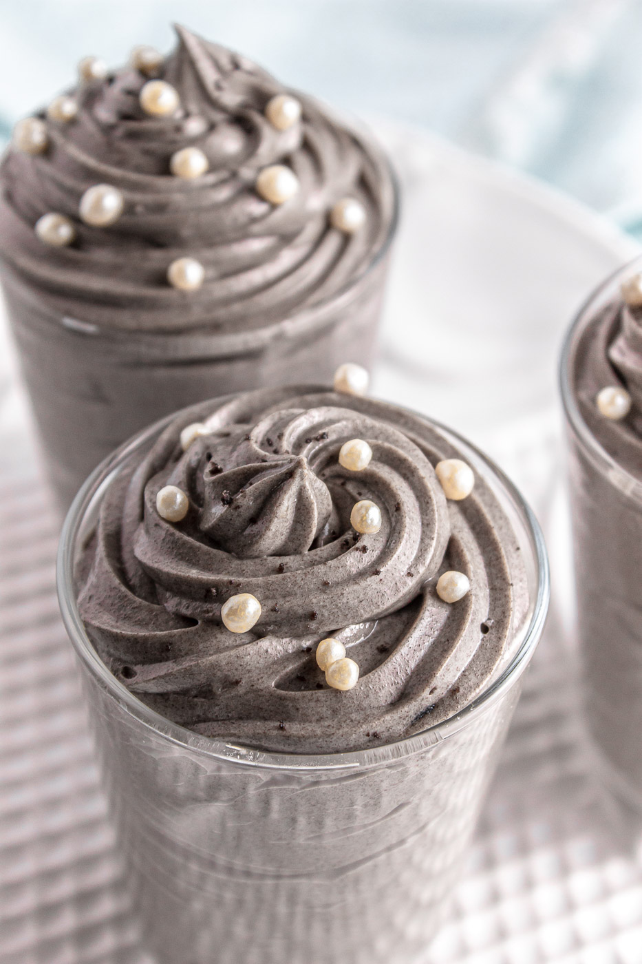 A closeup of glass jars that are filled with piped and swirled grey stuff dessert topped with white sprinkles