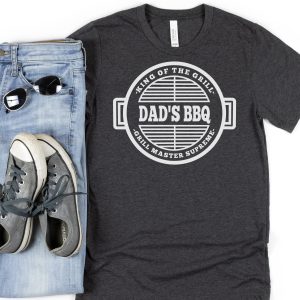 Dark grey Dad's BBQ shirt near jeans, shoes, and sunglasses.