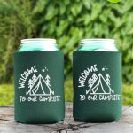 Two green can koozies with Welcome to Our Campsite design sitting on a tree stump in the forest