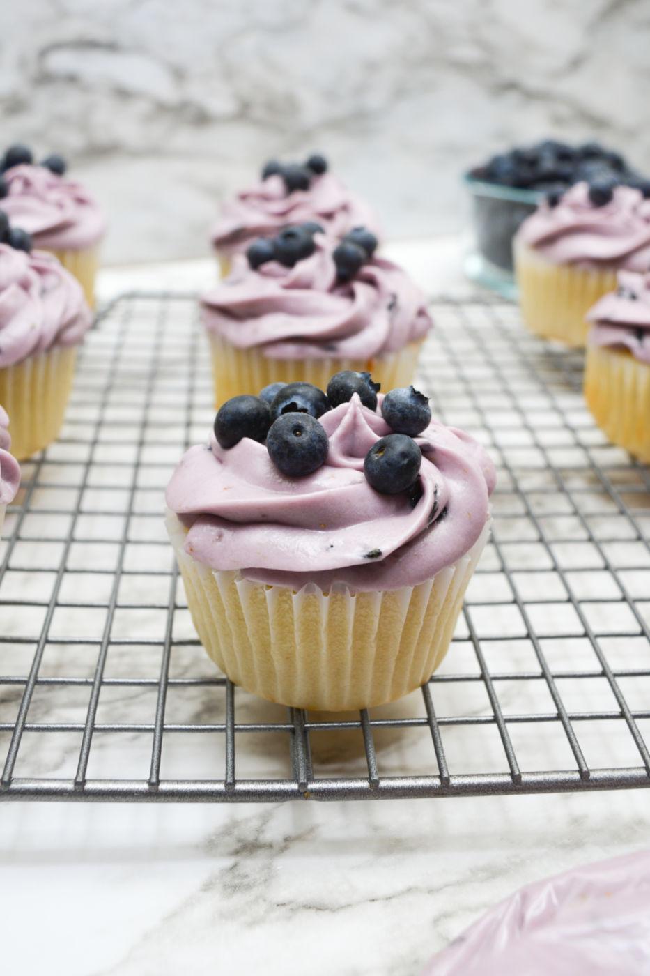 Close up of a frosted blueberry cupcake on a cooling rack